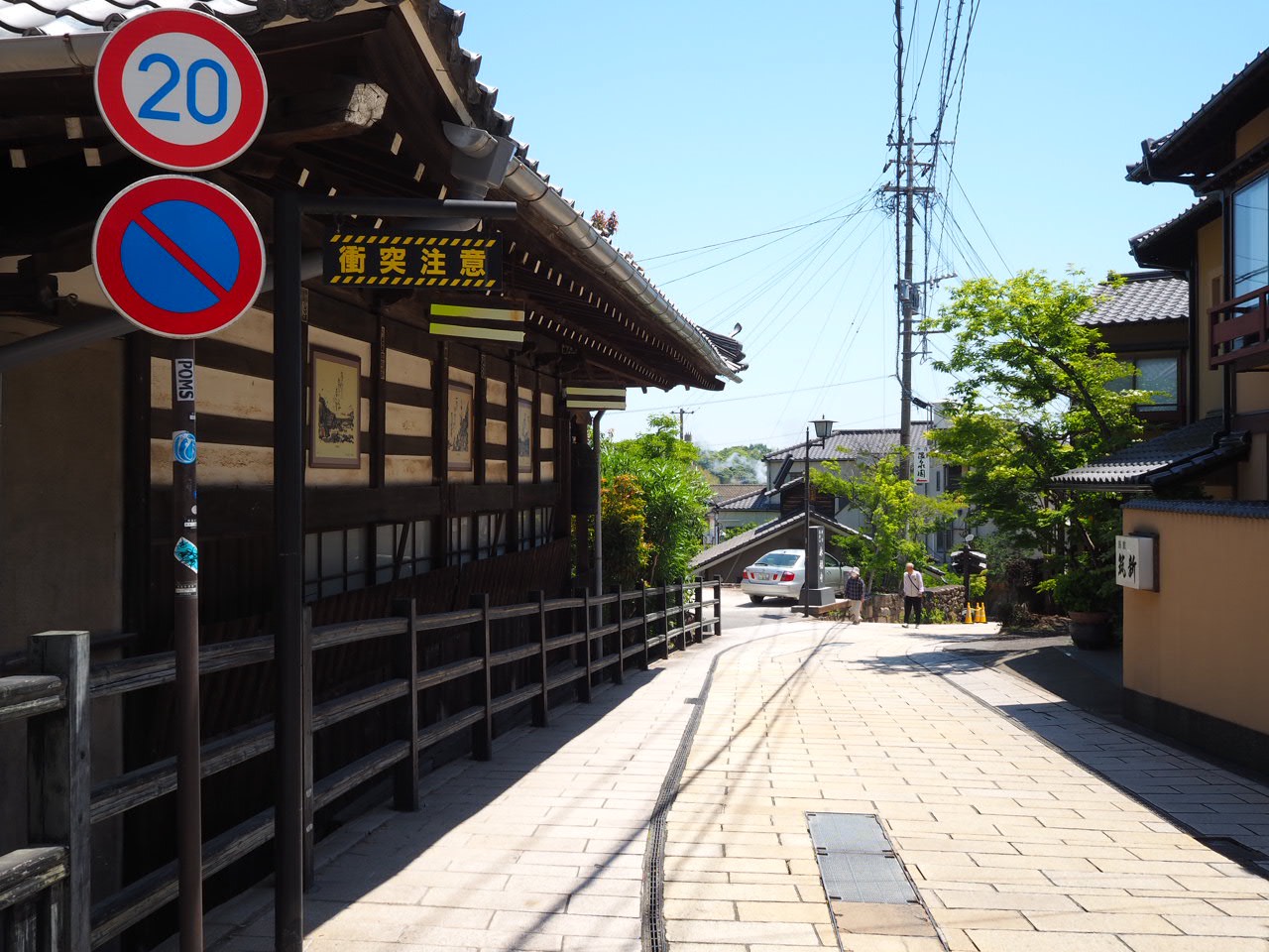 木造の建物と緑が並ぶ、日差しの中の別府の坂道